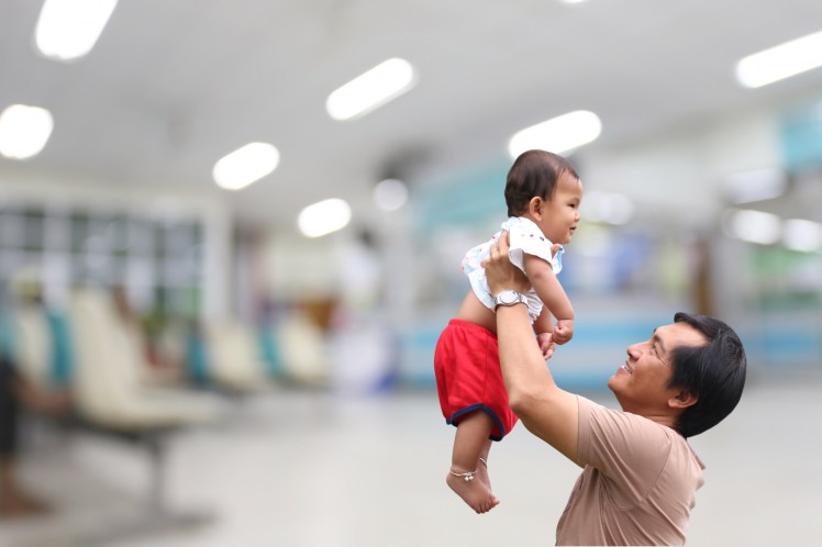Man håller upp en bebis mot blurrad bakgrund på ett sjukhus. Foto: Mostphotos
